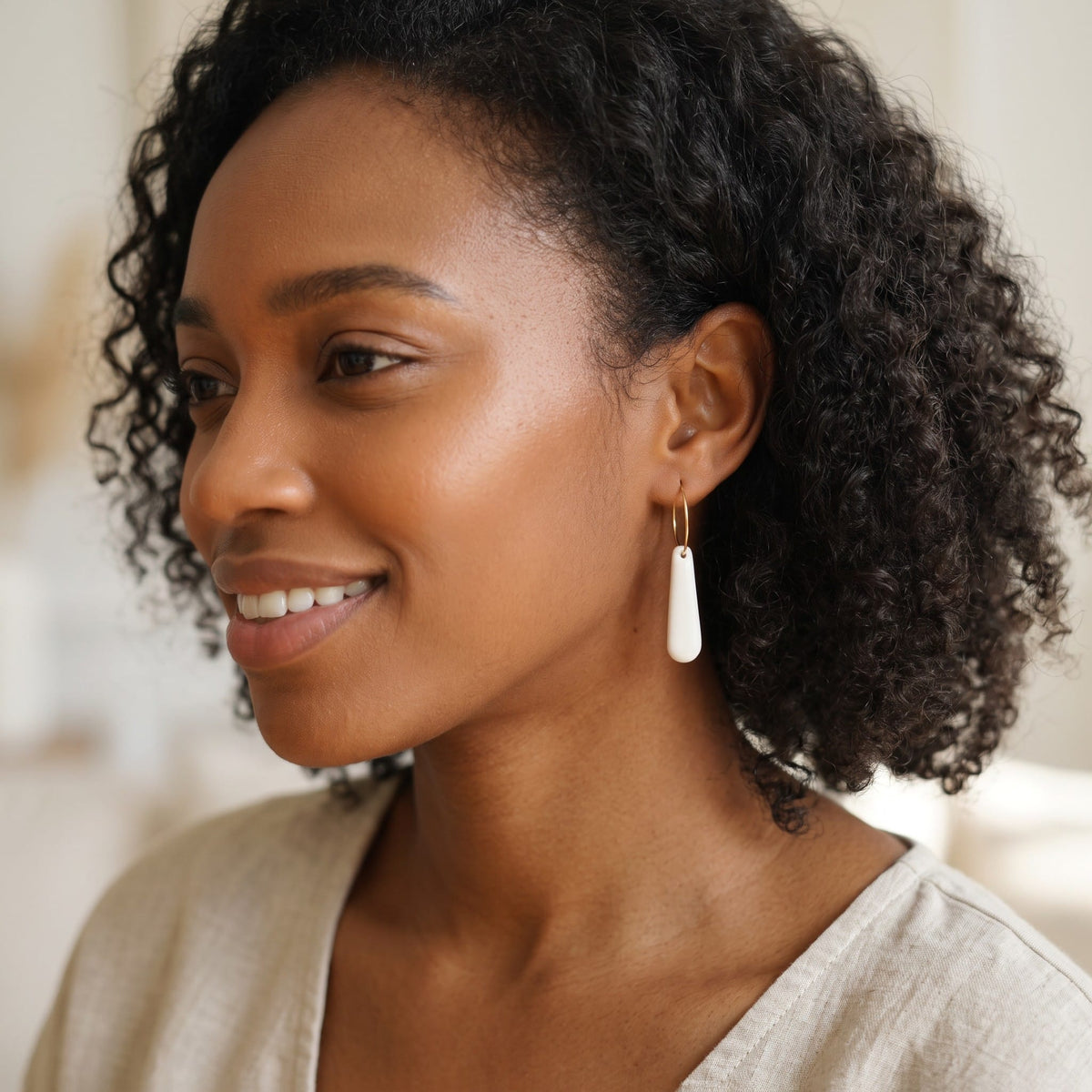 Profil portant les boucles d'oreilles créoles Aube en porcelaine blanche.