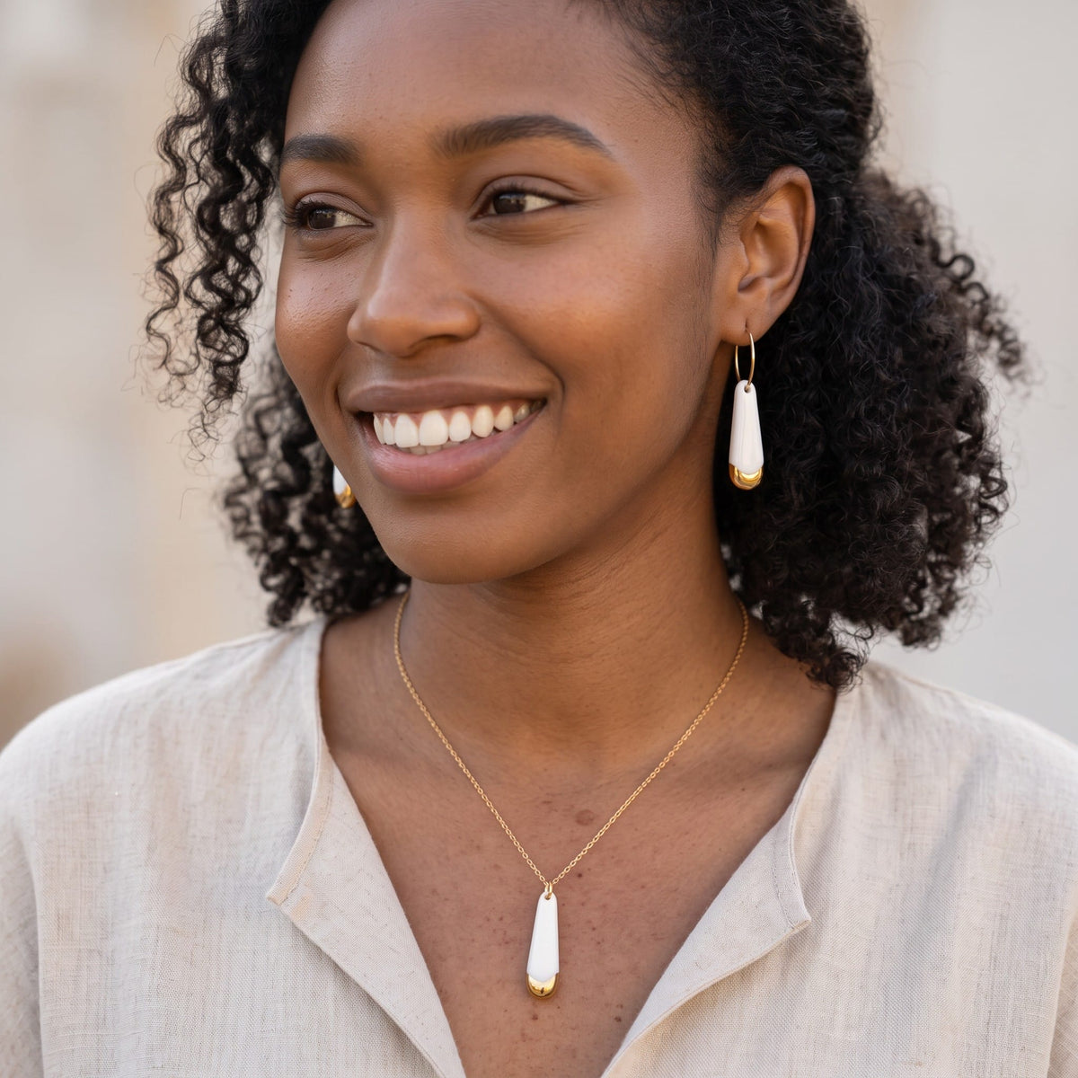 Collier pendentif Aube en porcelaine blanche et or porté avec les boucles d'oreilles de la collection Aube