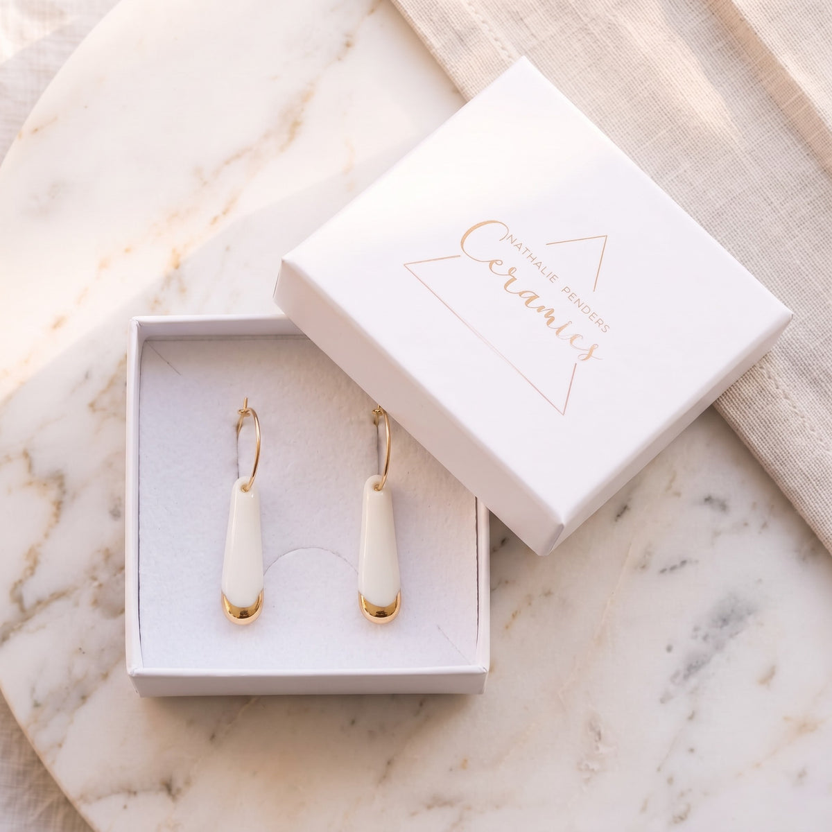 Boucles d'oreilles créoles Aube en véritable porcelaine blanche avec touche d'or dans son écrin.