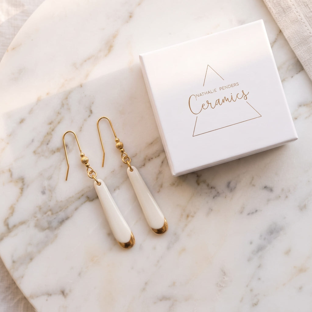 Boucles d'oreilles pendantes Aube en porcelaine blanche et or dans leur écrin