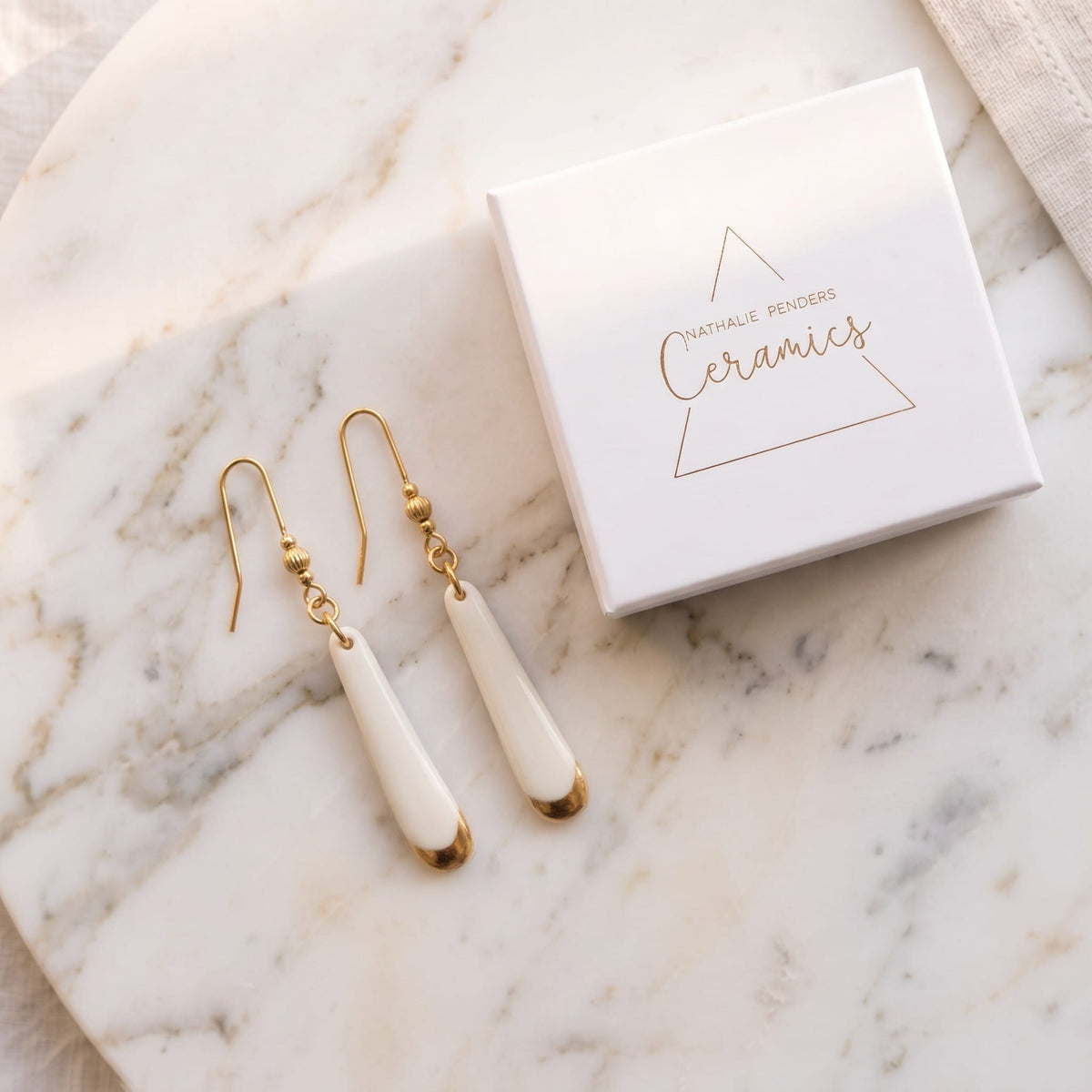 Boucles d'oreilles pendantes Aube en porcelaine blanche et or dans leur écrin