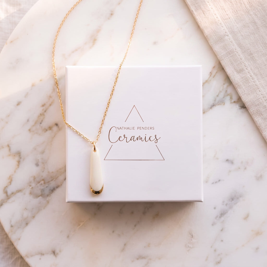 Collier pendentif Aube en porcelaine blanche et or présenté dans son écrin Nathalie Penders 