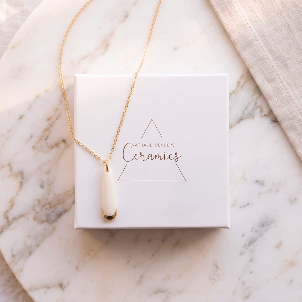 Collier pendentif Aube en porcelaine blanche et or présenté dans son écrin Nathalie Penders 