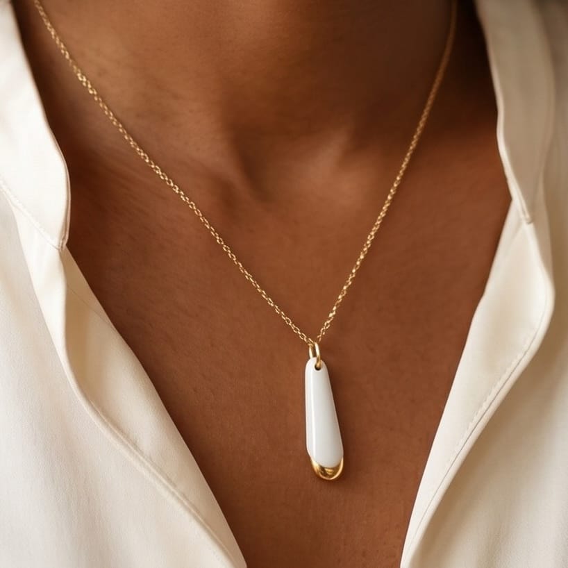 Gros plan du pendentif Aube en porcelaine blanche et or sur chaîne dorée