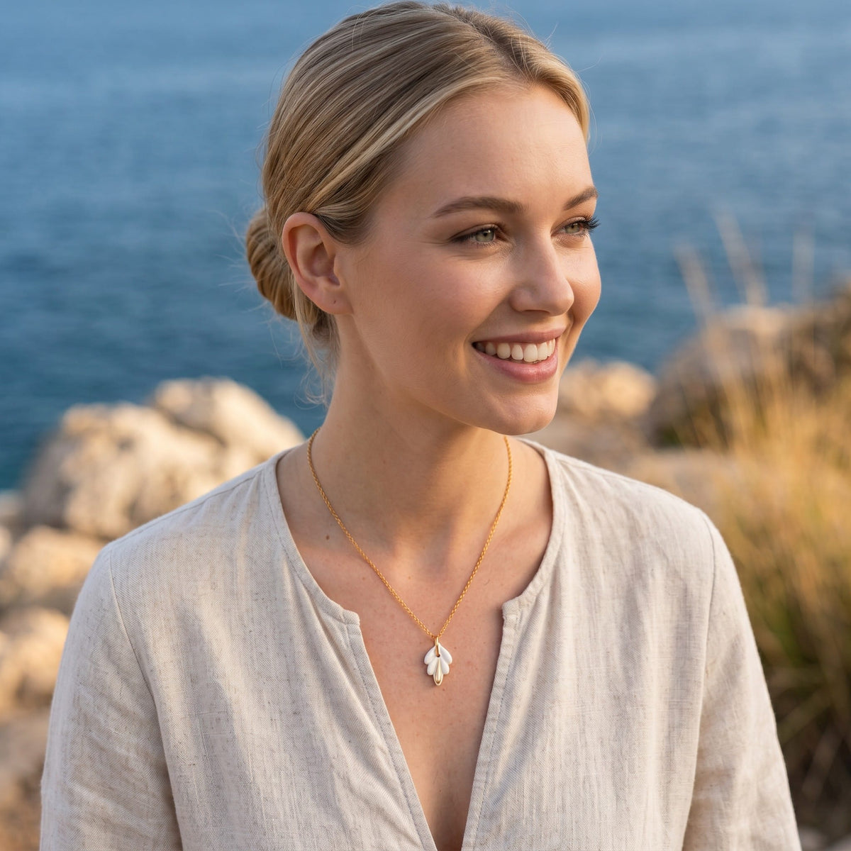 Collier pendentif lys porcelaine et or porté par une femme, atmosphère bord de mer